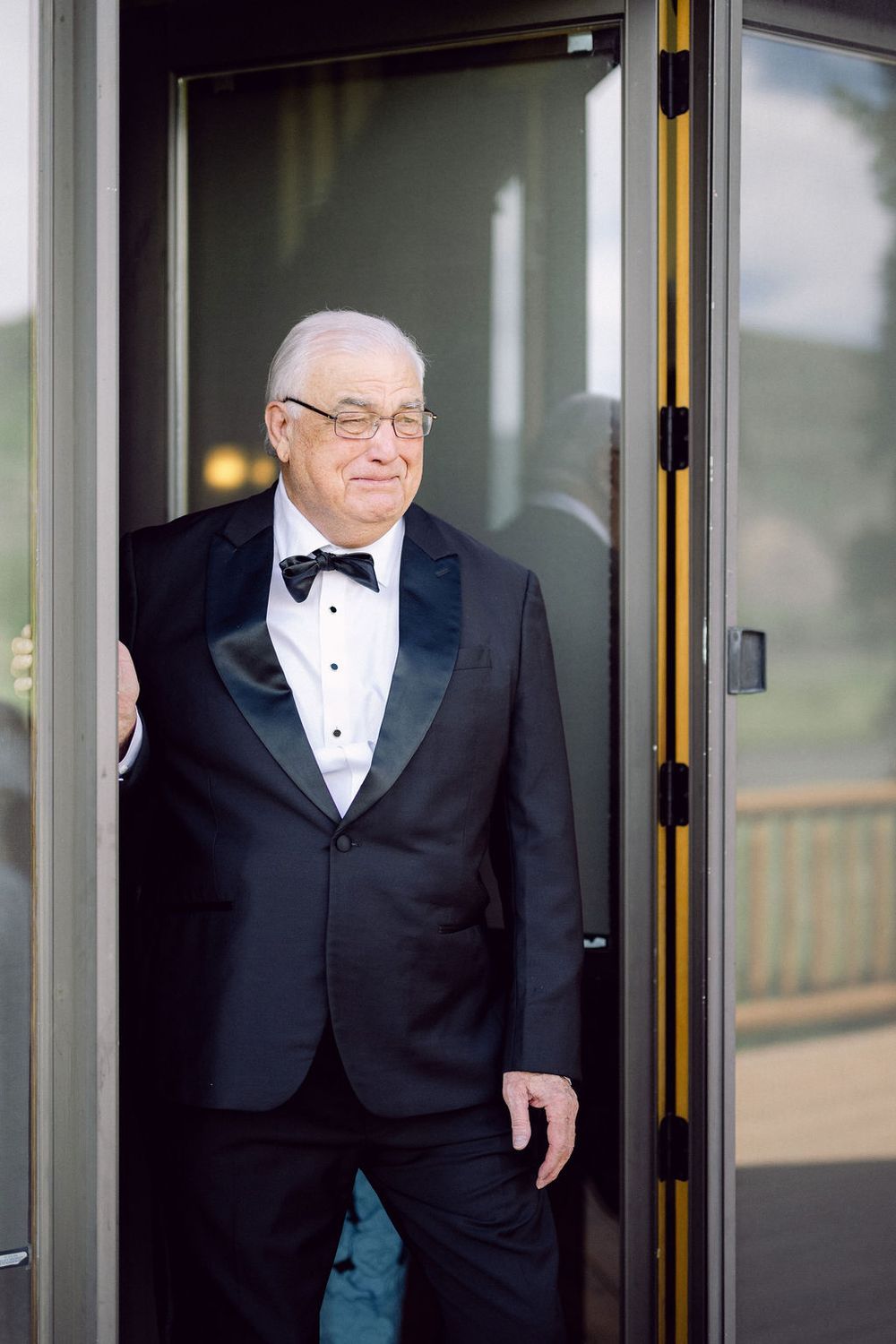 A person in a black tuxedo and bowtie emerges through a doorway.