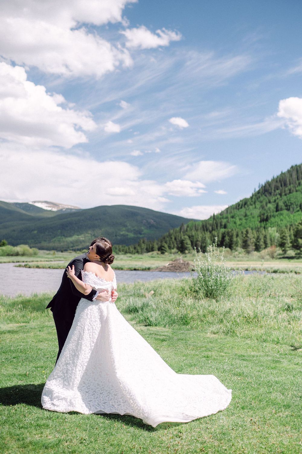 A couple shares a romantic moment in a white wedding dress against a backdrop of mountains and meadows in Colorado.