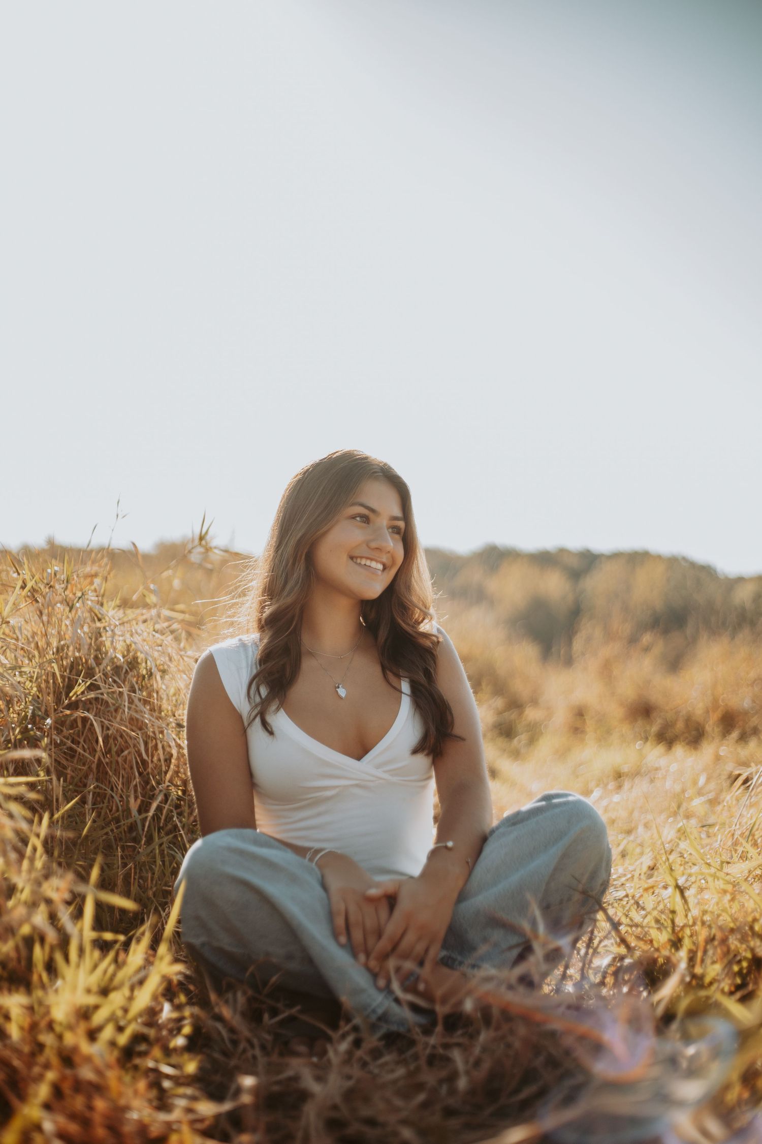 A person in white top and jeans relaxes in a golden field during sunset, creating a dreamy summer atmosphere.