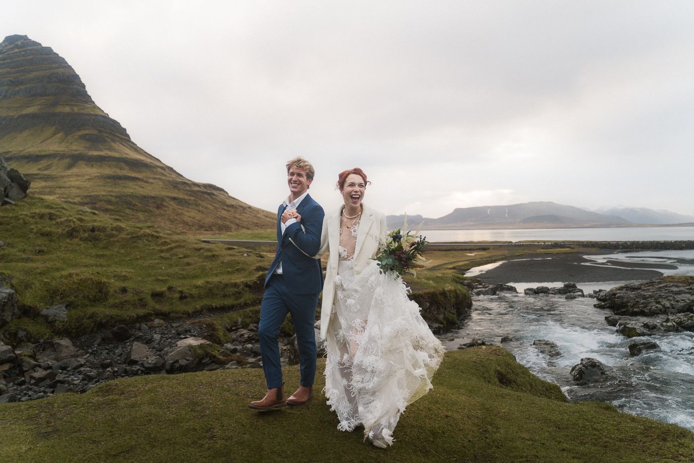 A happy couple running towards the camera in front of Kirkjufell.