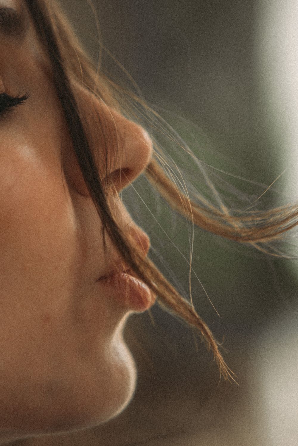 Close up profile view of lips and nose with wispy strands of hair floating in soft natural lighting.