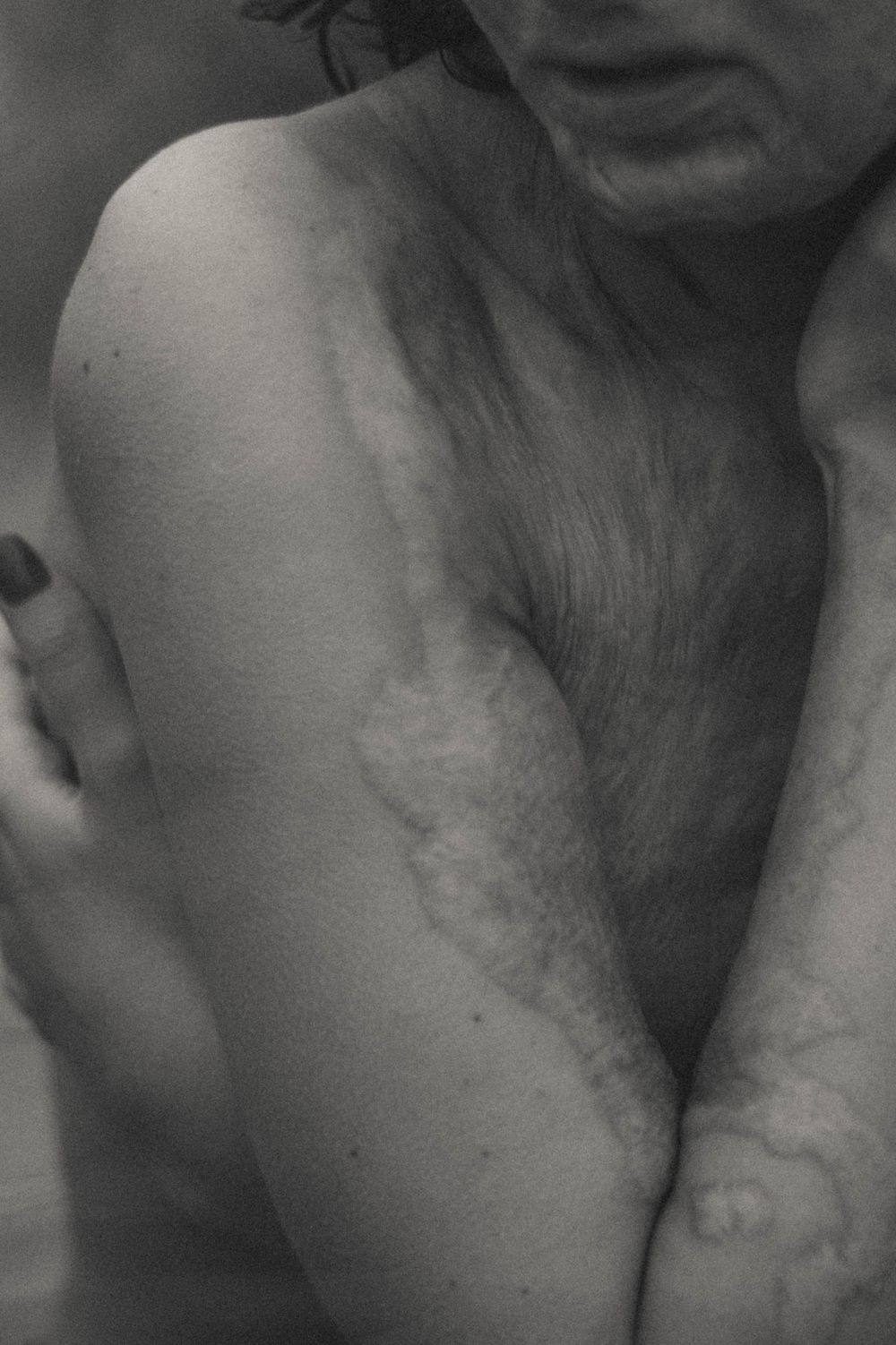 Black and white artistic photograph showing bare skin and shadows in an intimate close-up composition.