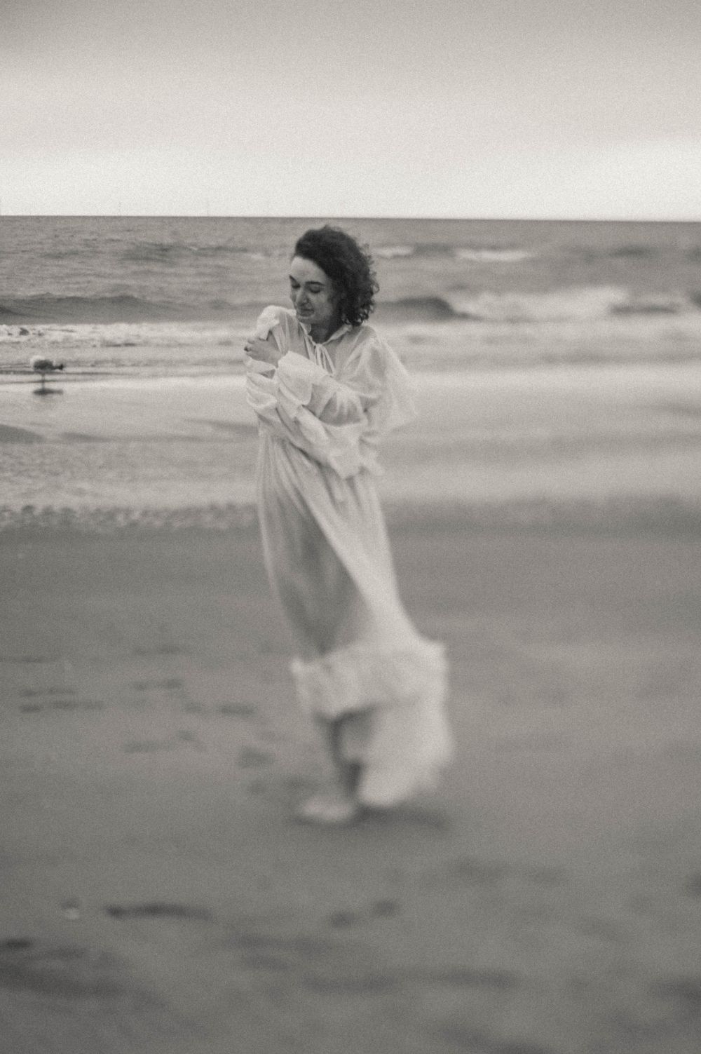 A person in a white dress dances joyfully on a misty beach in black and white photography.