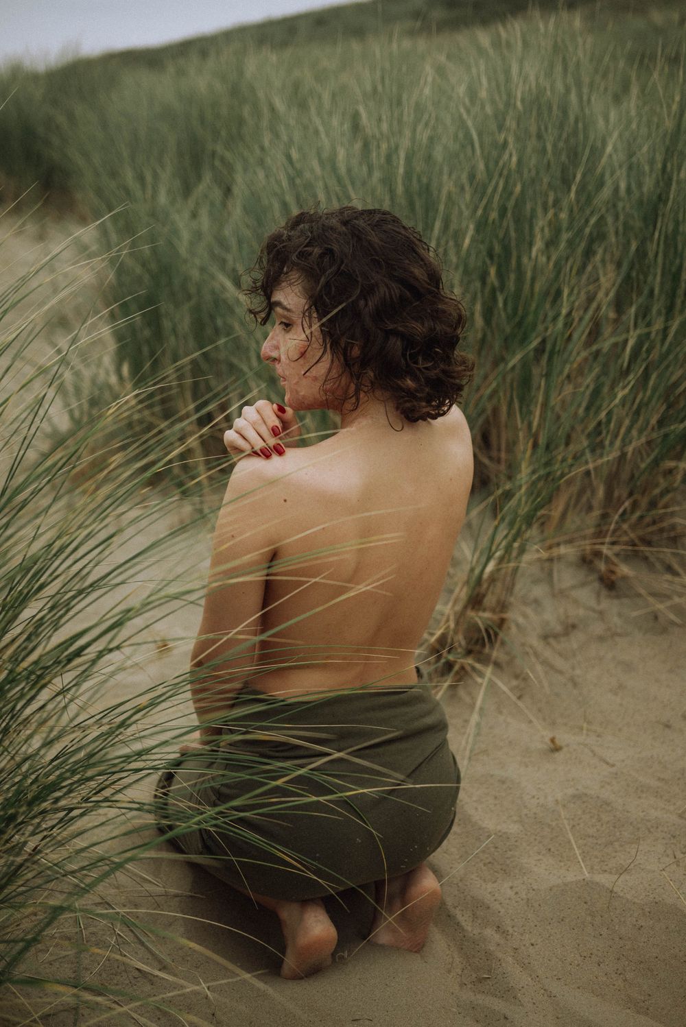Artistic portrait series of a person sitting in beach grass wearing dark clothing against a natural coastal backdrop.