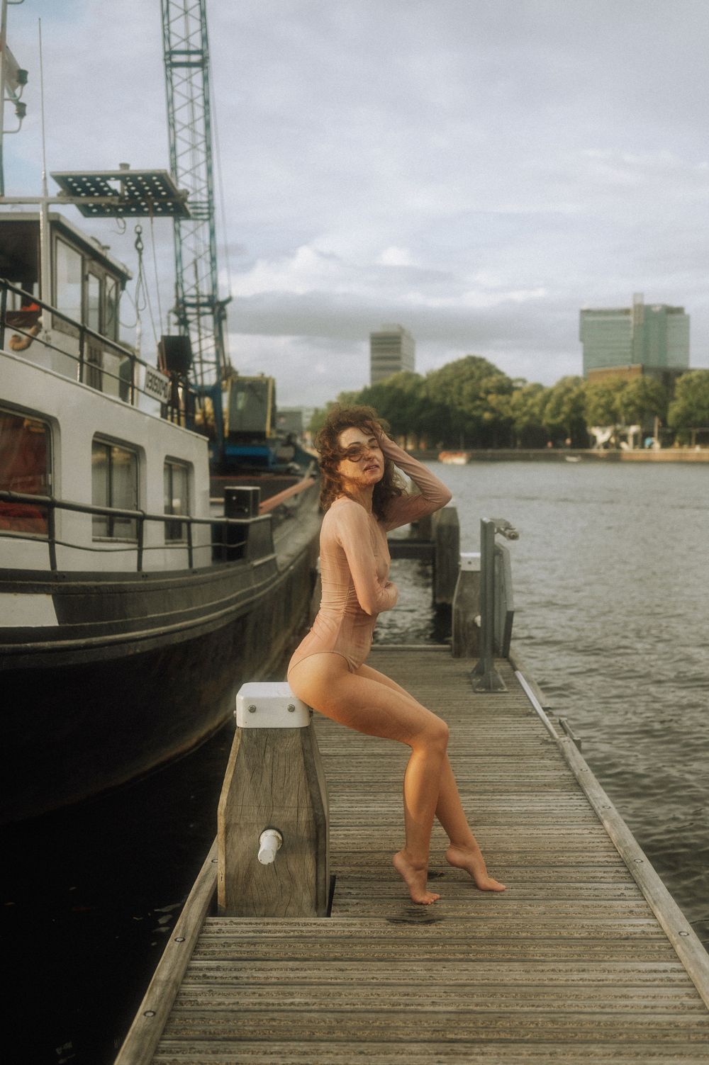 A series of photos showing someone posing on a wooden dock by boats and water on an overcast day.