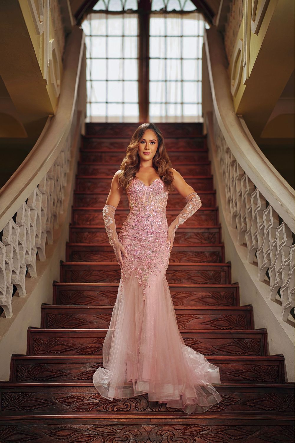 A flowing pink formal dress captured on vintage wooden stairs with decorative white banisters.
