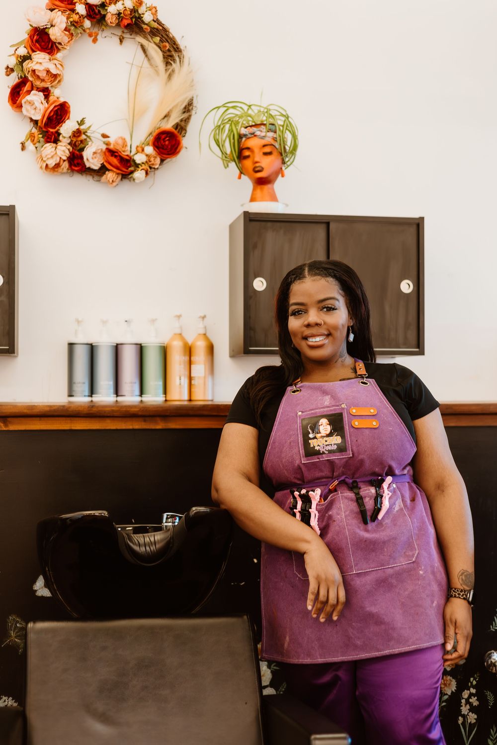 A small business owner wearing a purple apron smiles while working in their shop interior.