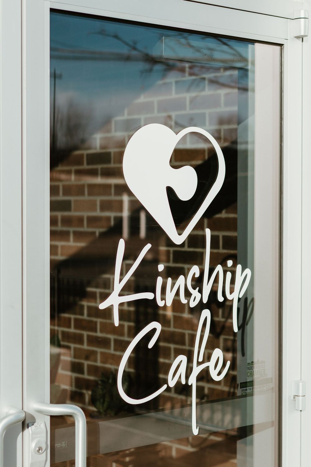 White cursive text reading 'Kinship Cafe' displayed on glass windows of a brick building exterior.