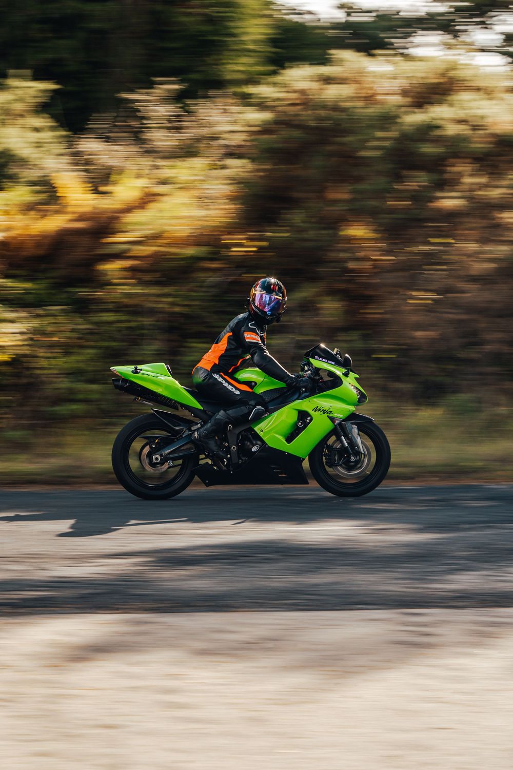 Bright green sport motorcycle in motion on a curved road with motion blur and autumn foliage in background.