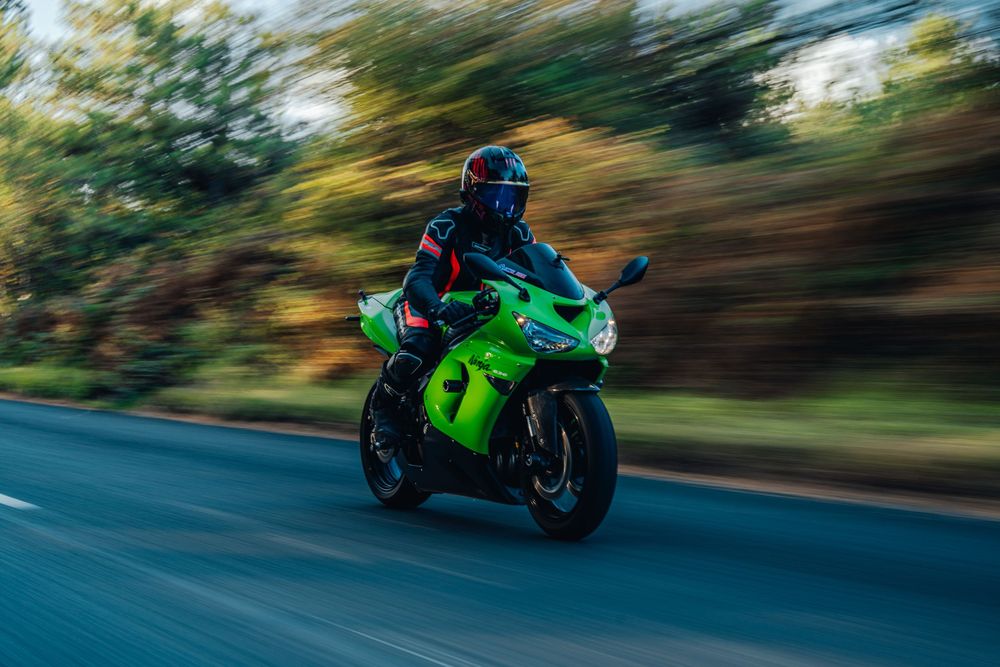 Green motorcycle rider speeding down a curvy road with motion blur creating a dynamic racing effect.