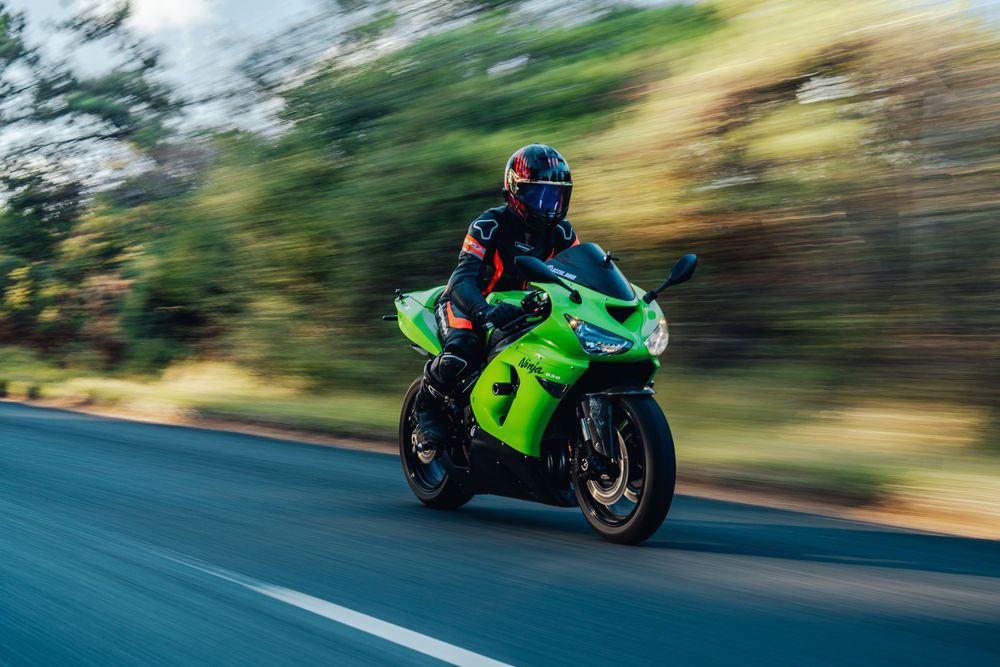 Motorcyclist in bright green sport bike racing along a winding mountain road at high speed.