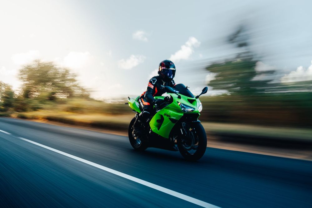A motorcyclist rides a bright green sports bike at high speed on a blurred motion highway during daytime.