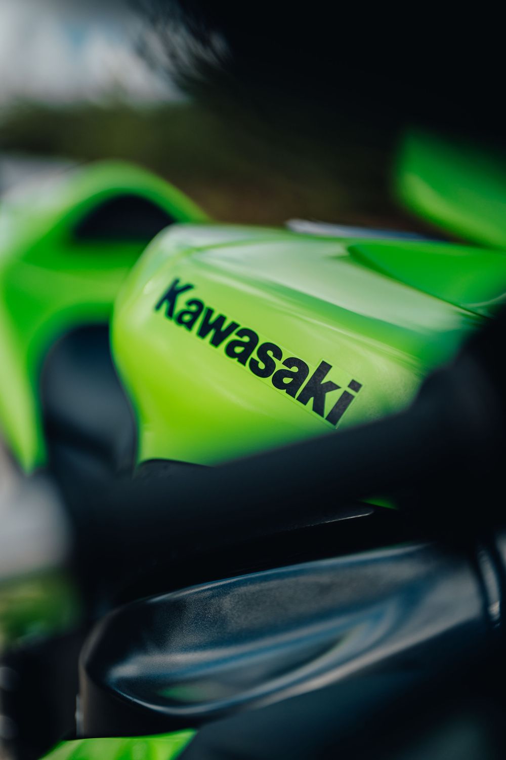 Close-up macro shot of a green Kawasaki motorcycle body panel showing the brand name lettering in selective focus.