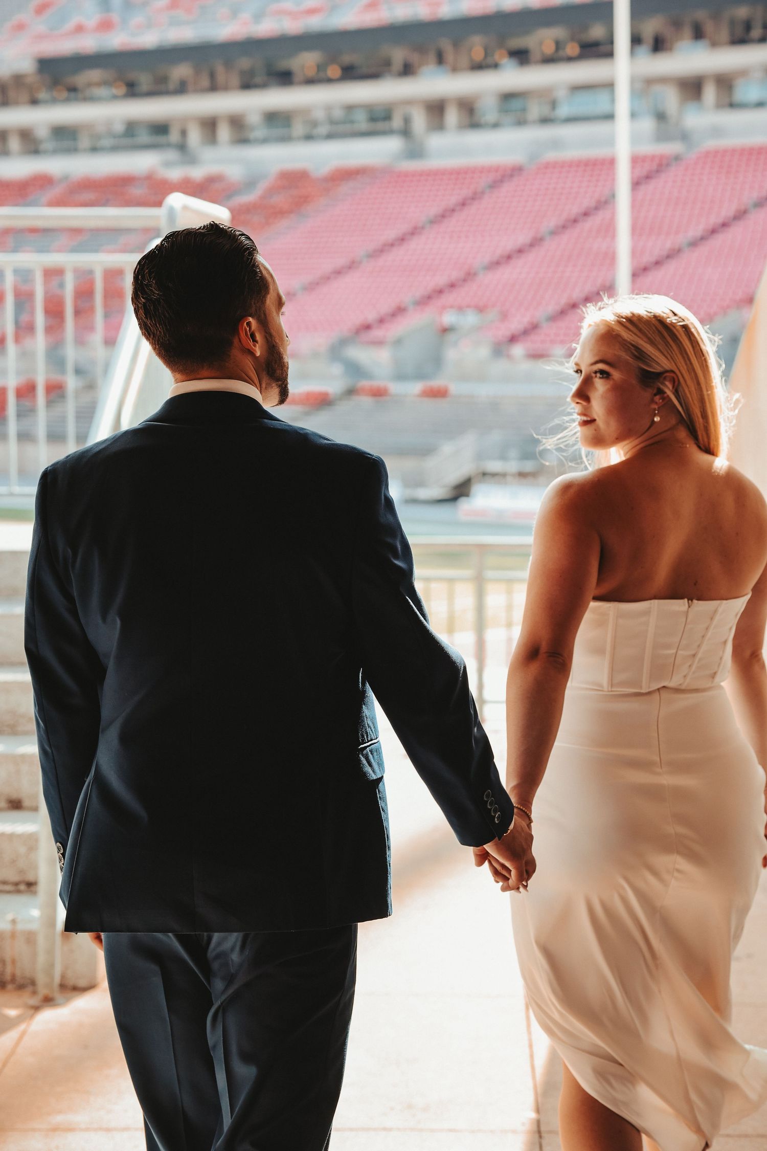 A bride and groom holding hands while walking through a stadium venue.