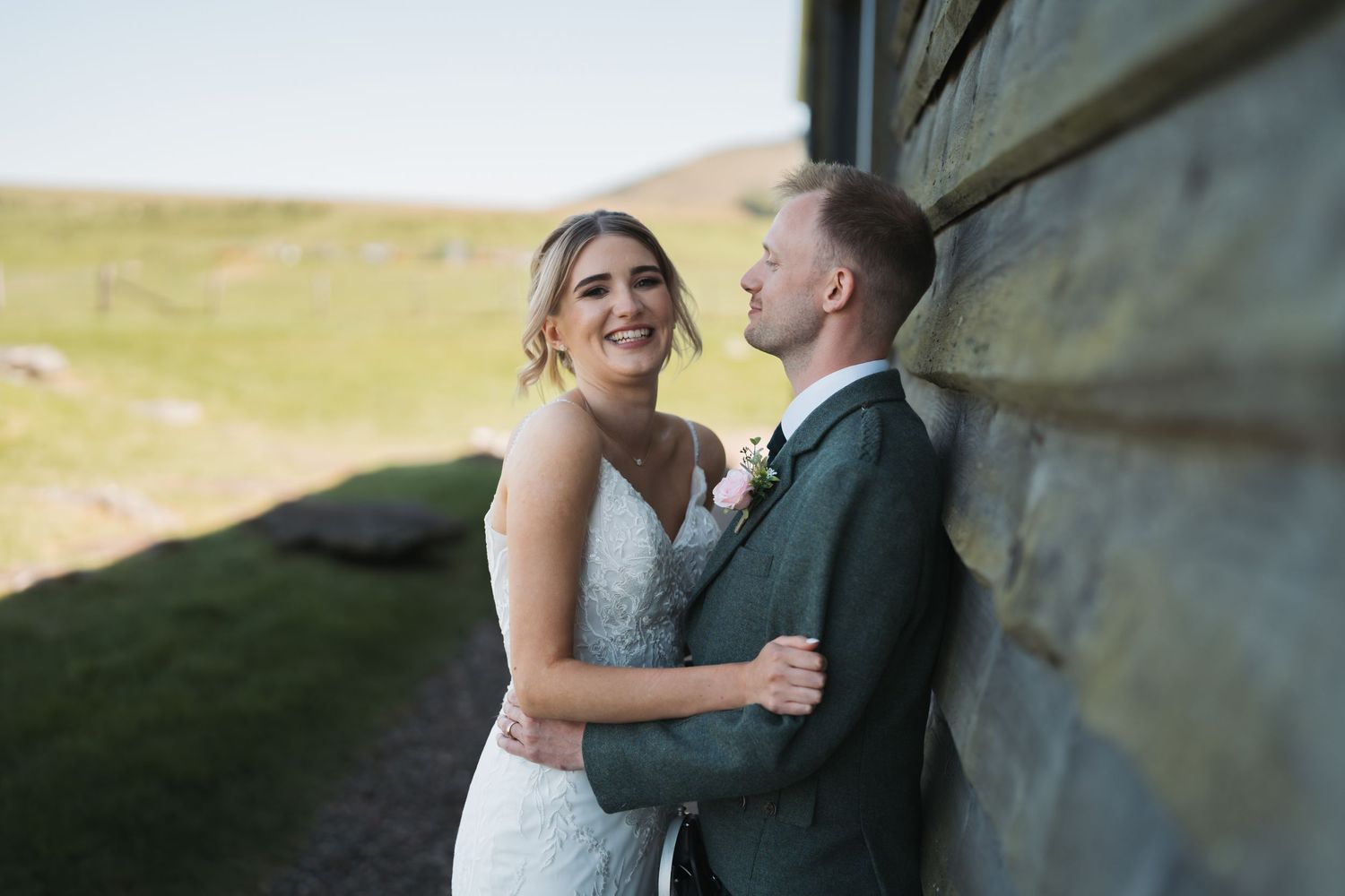 A couple shares an intimate moment against a rustic wooden wall during their outdoor wedding celebration.