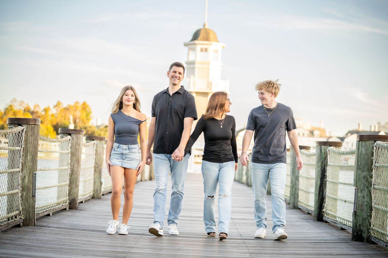 Family members walk together holding hands on a wooden pier during a casual outdoor photo session.