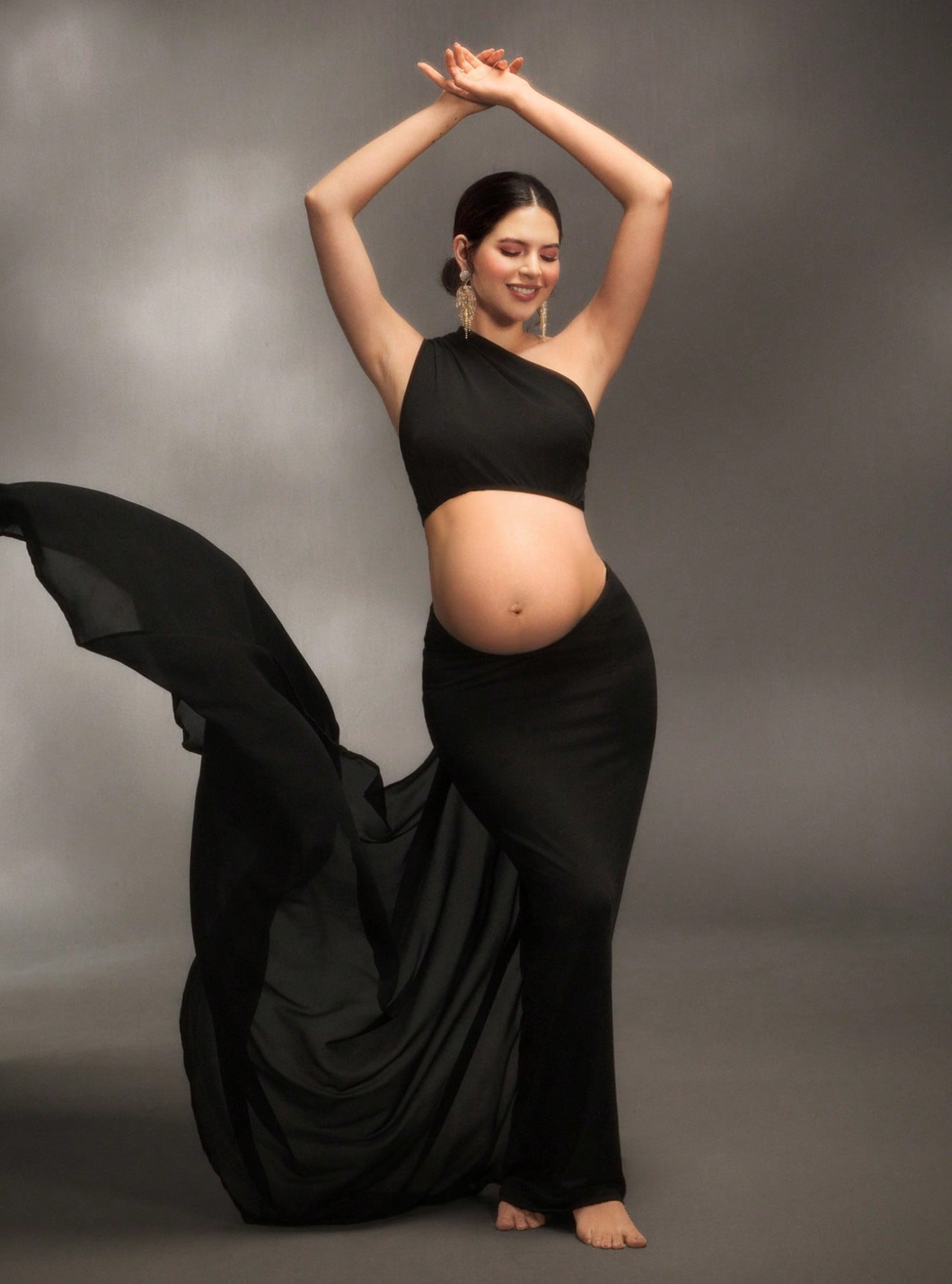 Dramatic maternity dance poses in black dress against dark background.