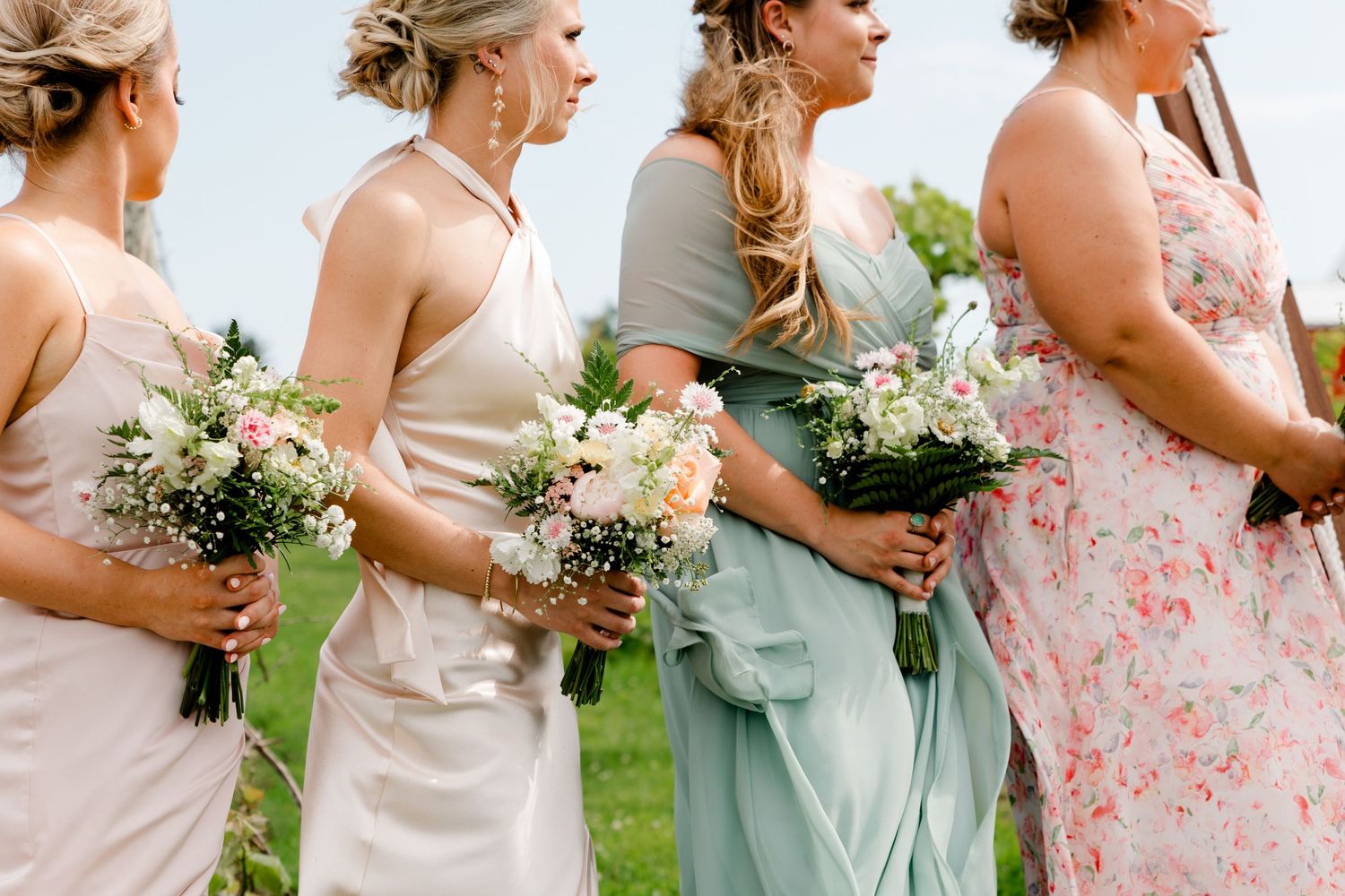 Bridesmaids in mismatched pastel dresses holding romantic white and pink floral bouquets.