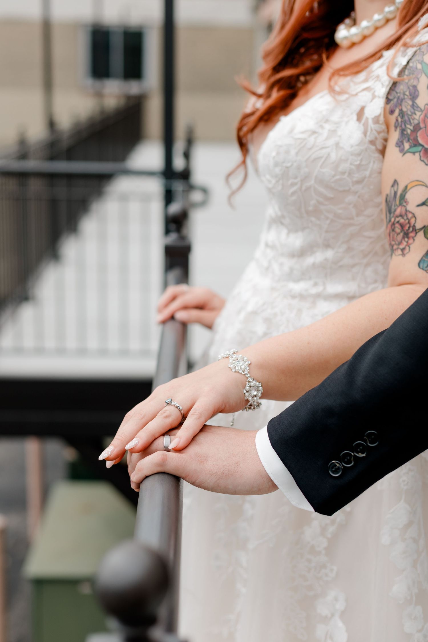 Close-up of bride and groom holding hands on railing, showcasing wedding rings and crystal bracelet.