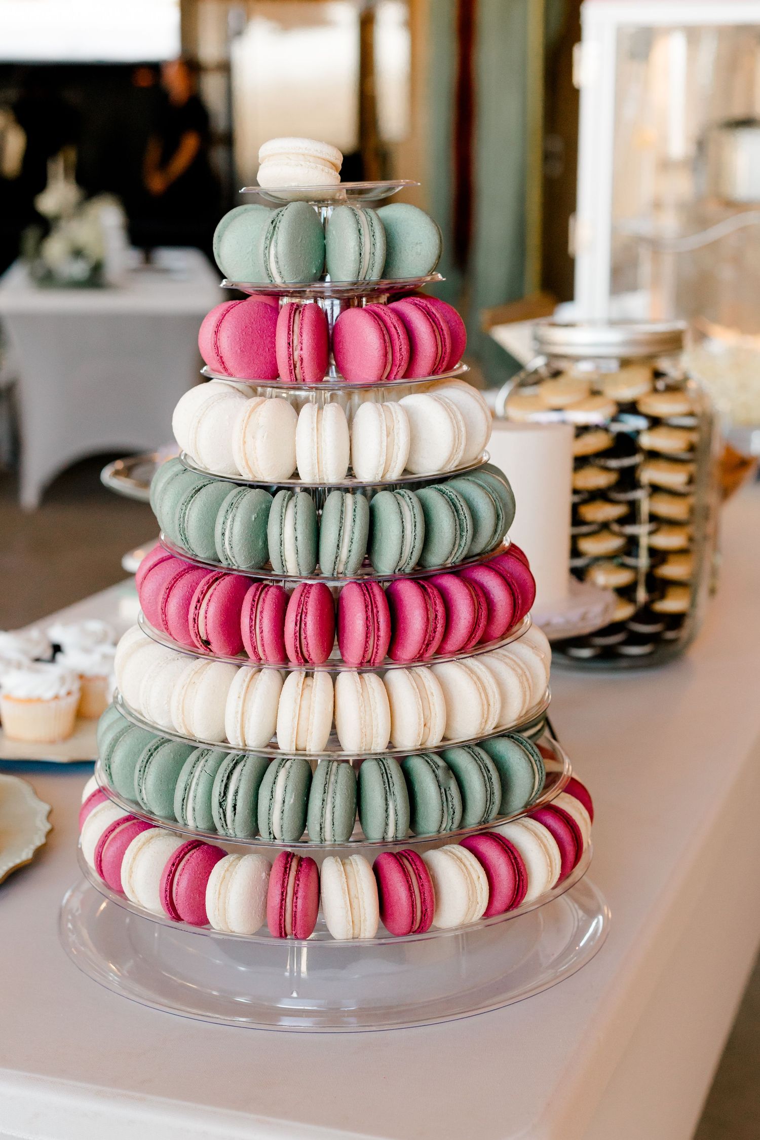 Elegant macaron tower display with pink, white, and green macarons stacked in tiers on a clear acrylic stand.