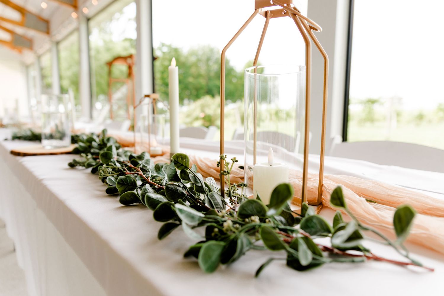 Elegant wedding table centerpiece with greenery garland and gold geometric candle holders.