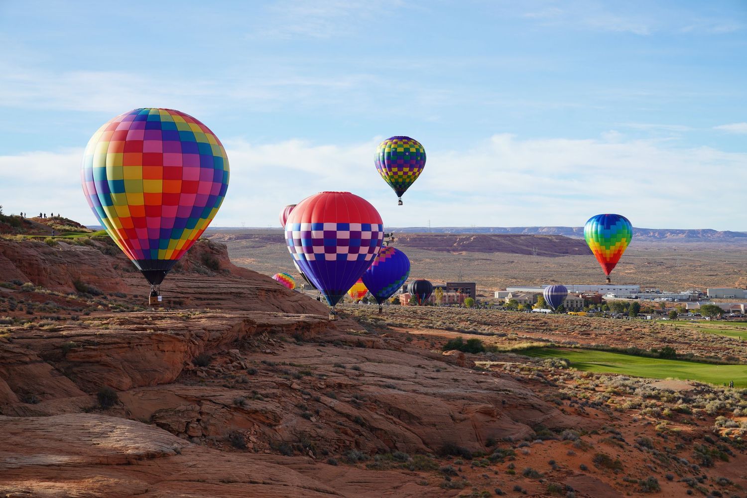 Colorful hot air balloons float against blue sky over desert landscape near red rock formations in Page, Arizona.