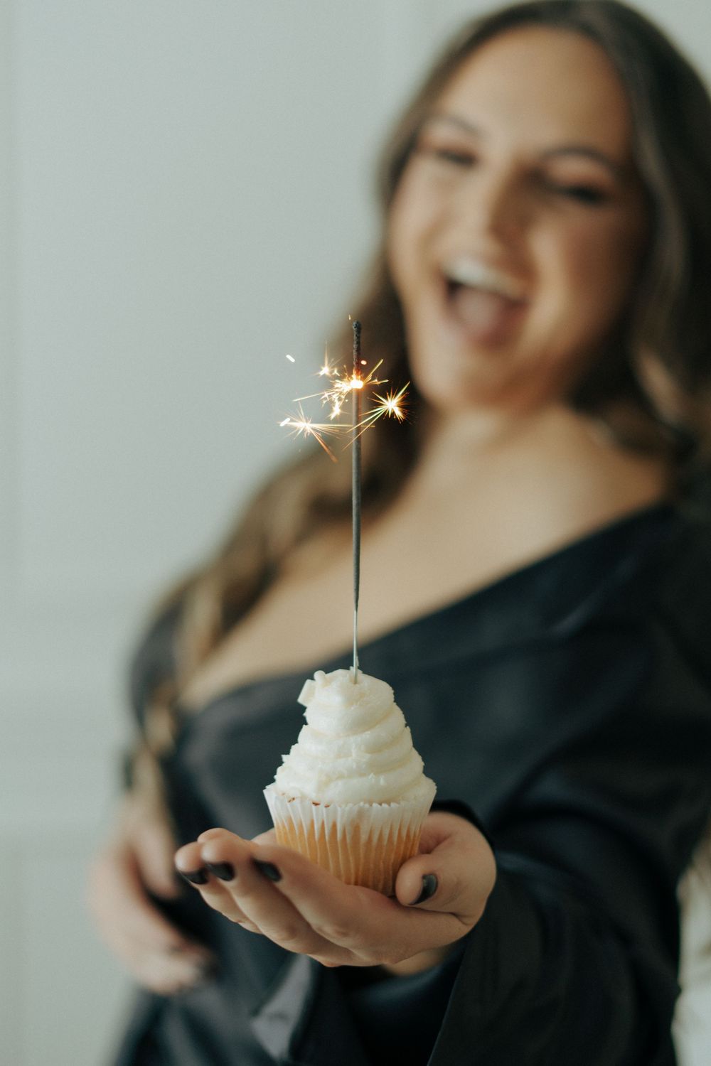 A person in black holds a white frosted cupcake with a sparkler on top in a series of celebratory photos.
