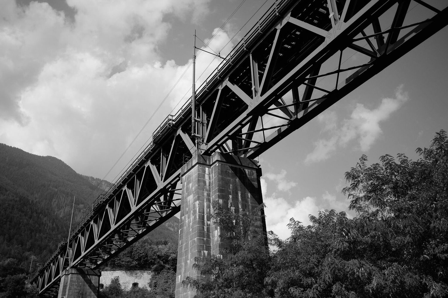 Low angle view of a steel railway bridge with concrete supports in black and white photography.