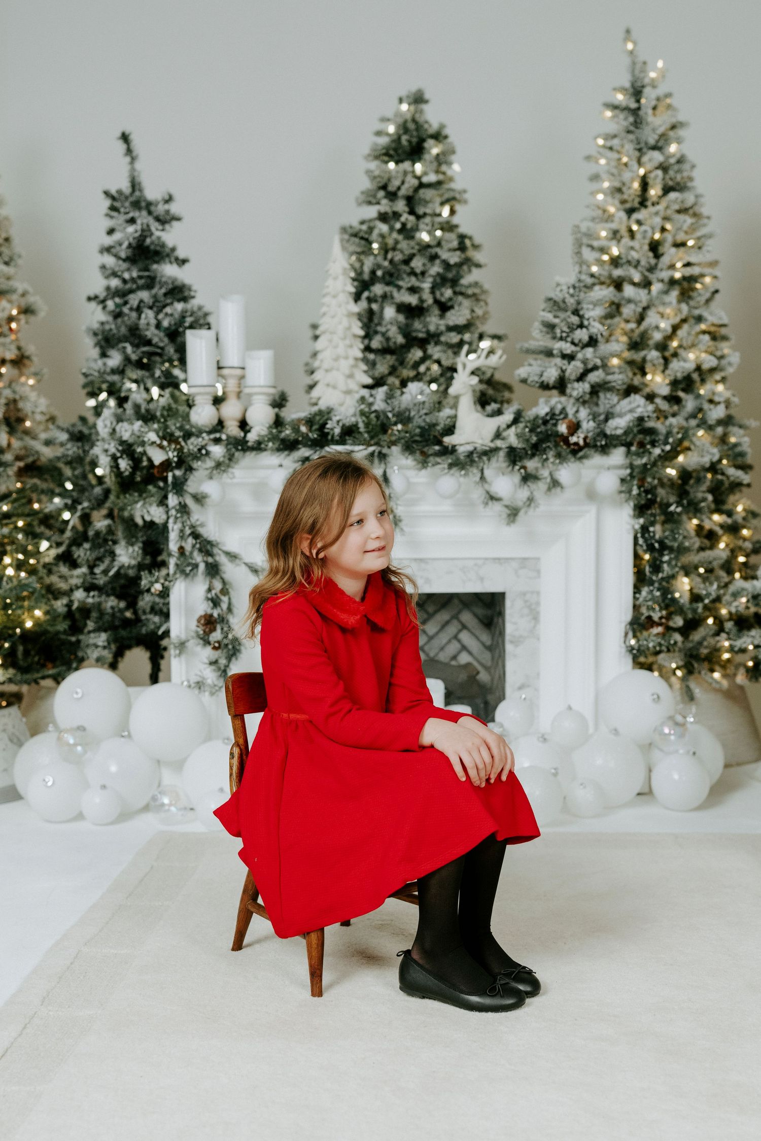 Holiday photo session with white Christmas trees, lights, and a red sweater against a snowy white backdrop.