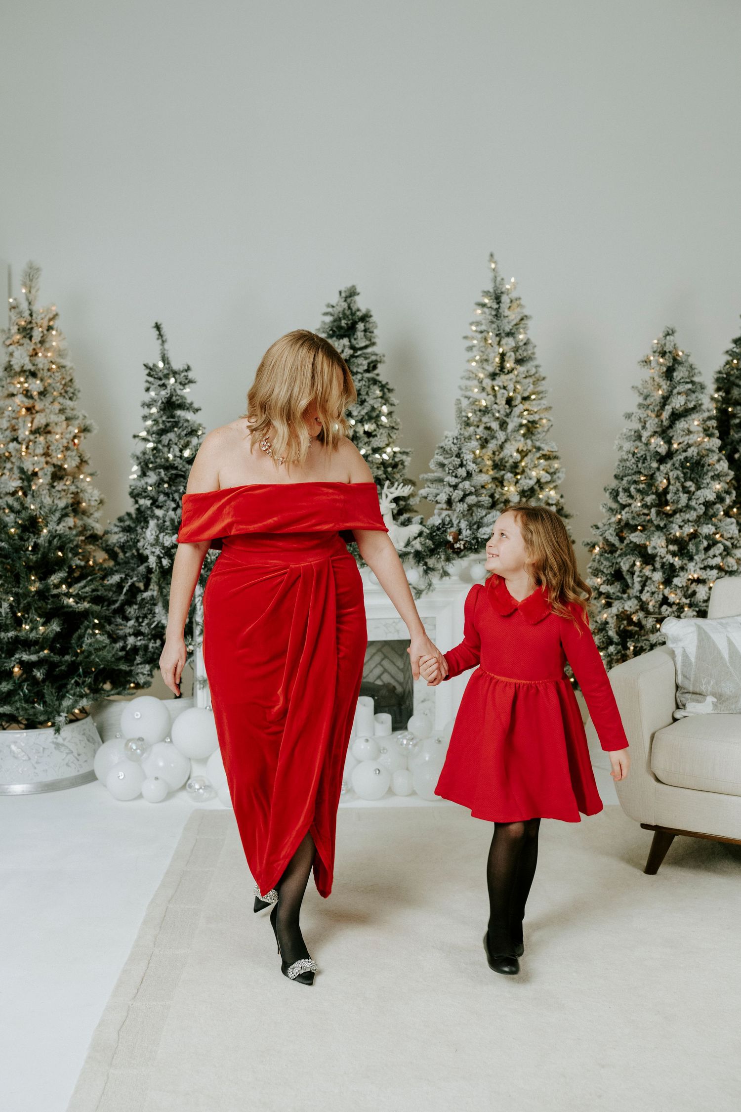 Two figures in matching red holiday dresses dance together in front of snow-covered Christmas trees.