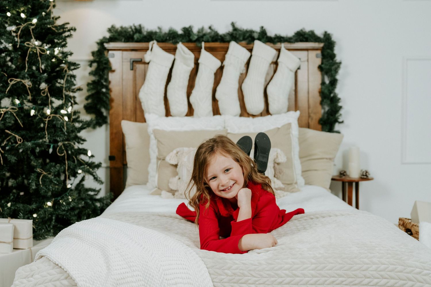 Person in red sweater relaxing on white bedding with Christmas decor in background.