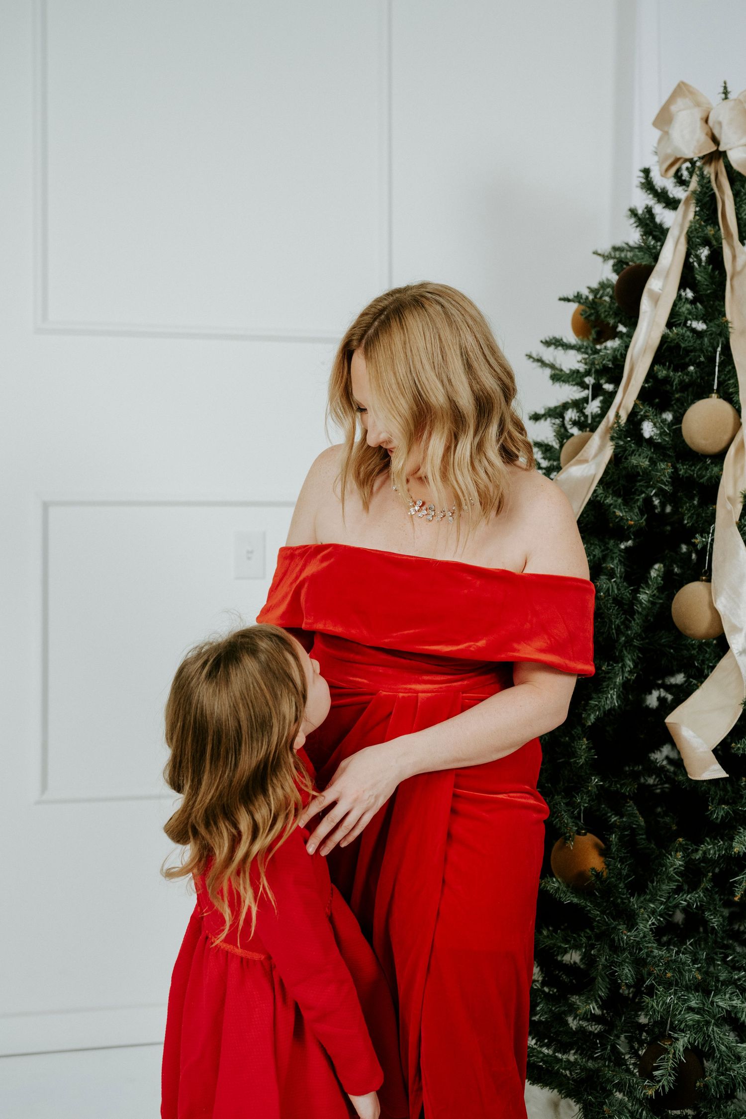 A series of photos showing people in red dresses decorating a Christmas tree against a white wall.