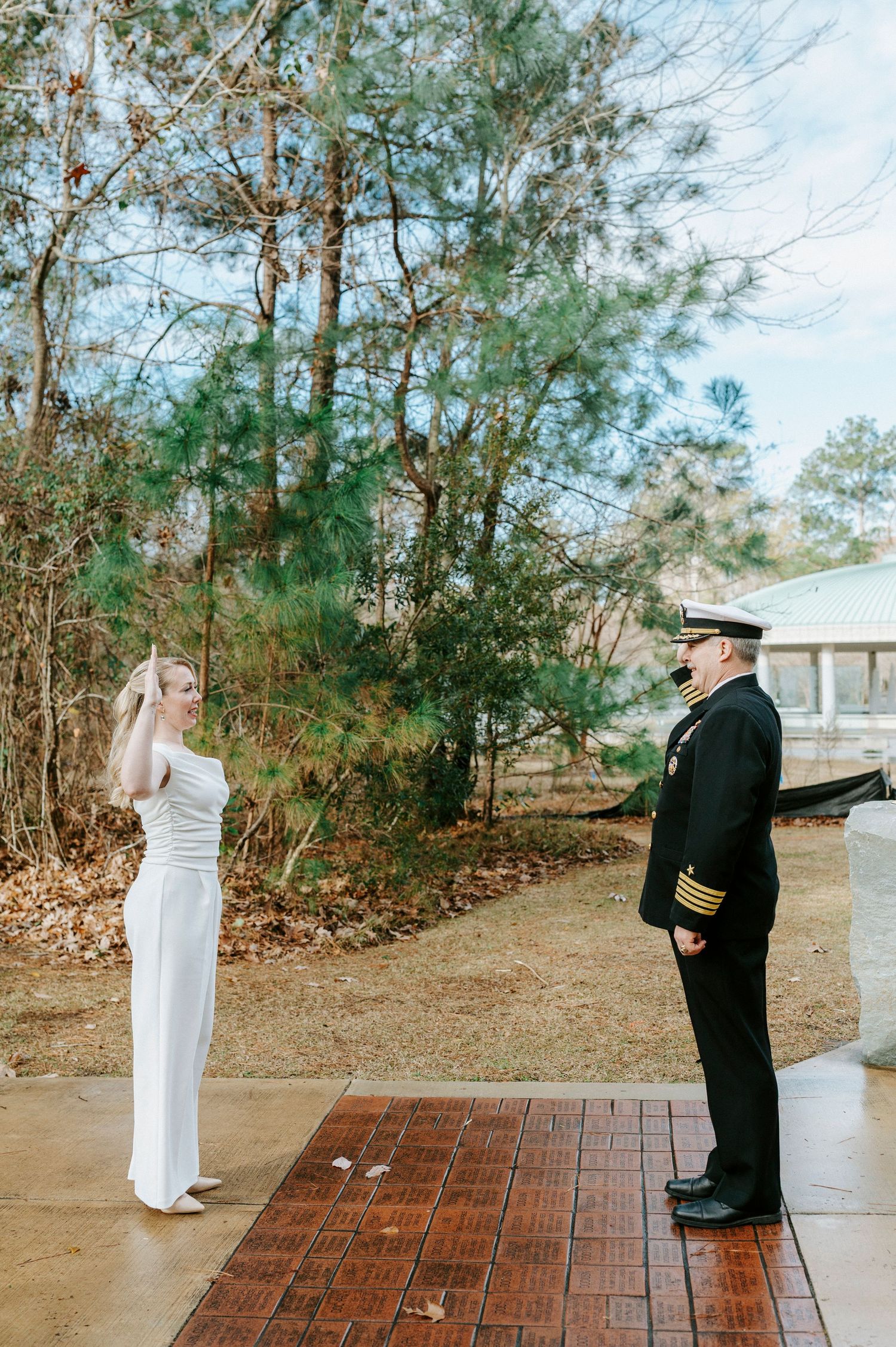 A couple shares an intimate first look moment on a brick patio surrounded by trees.