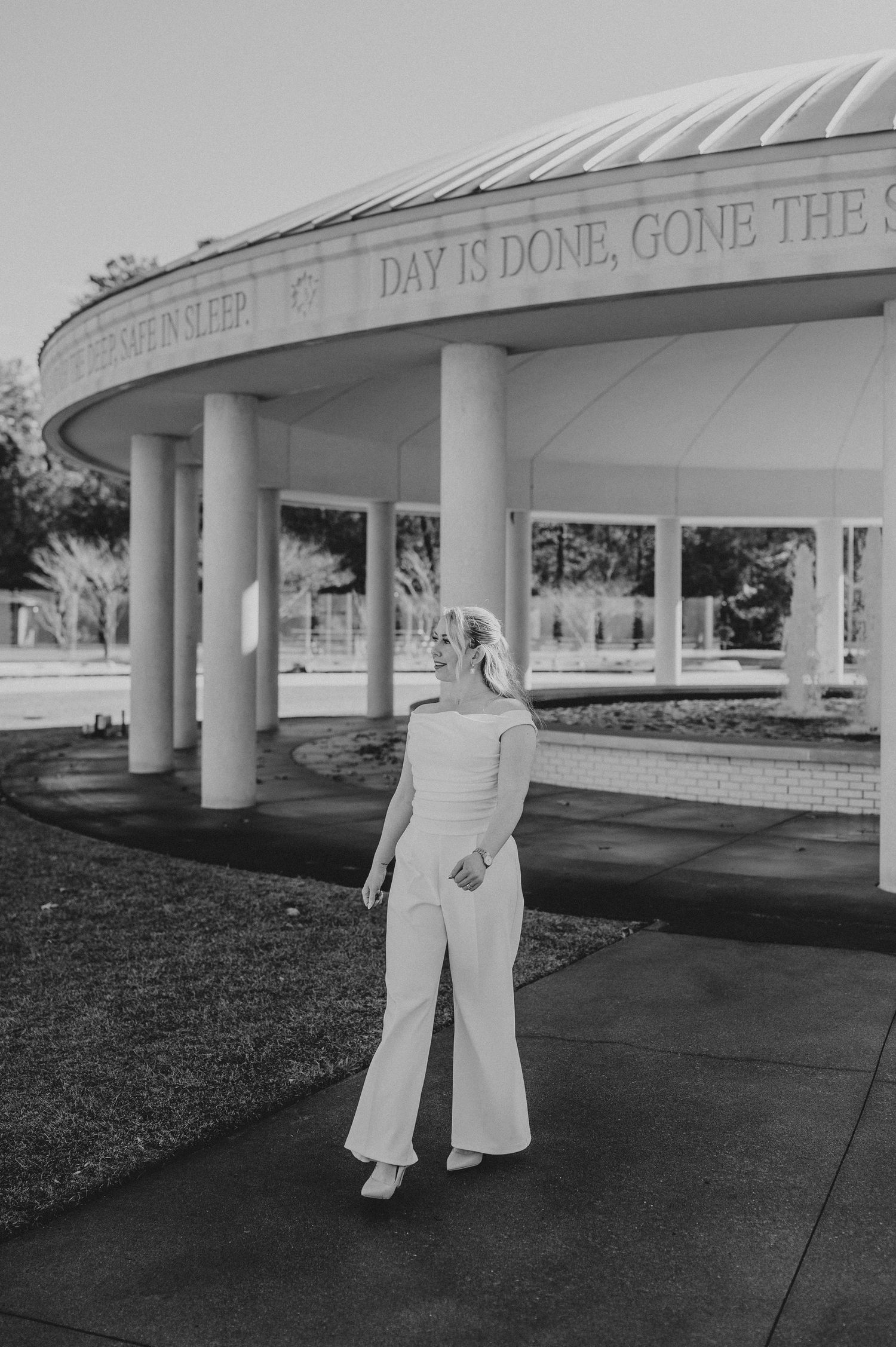 A couple poses together beneath a covered walkway with white columns at sunset.