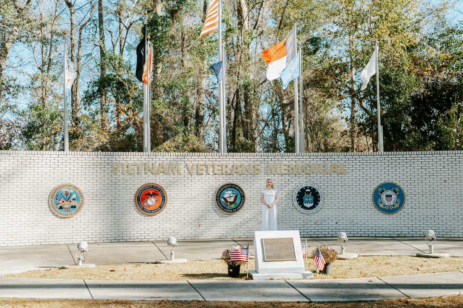 A row of military service branch emblems mounted on a white brick wall at a memorial or veterans site.