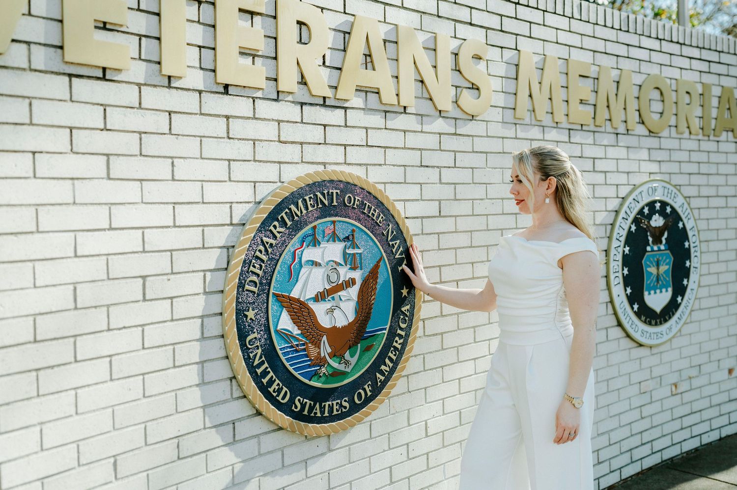 A white brick wall decorated with circular emblems and plaques forms part of a memorial display.