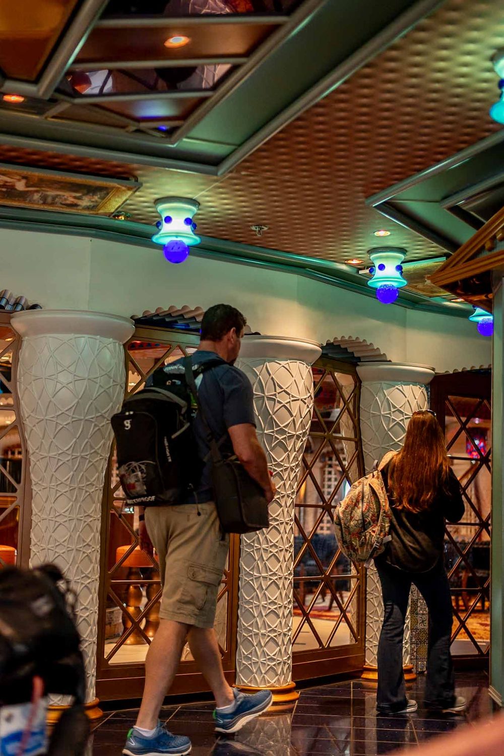 Interior view of a cruise ship hallway with decorative white columns and blue accent lighting.