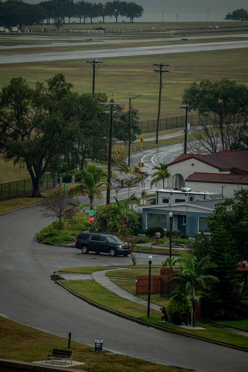 Aerial view of a residential area with curved roads, palm trees and buildings near an airport runway.