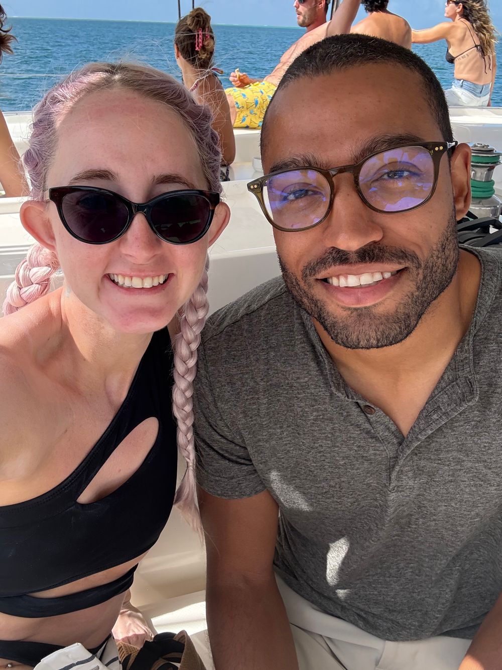A couple takes selfies together on a sunny beach day, showing bright smiles and ocean views in the background.