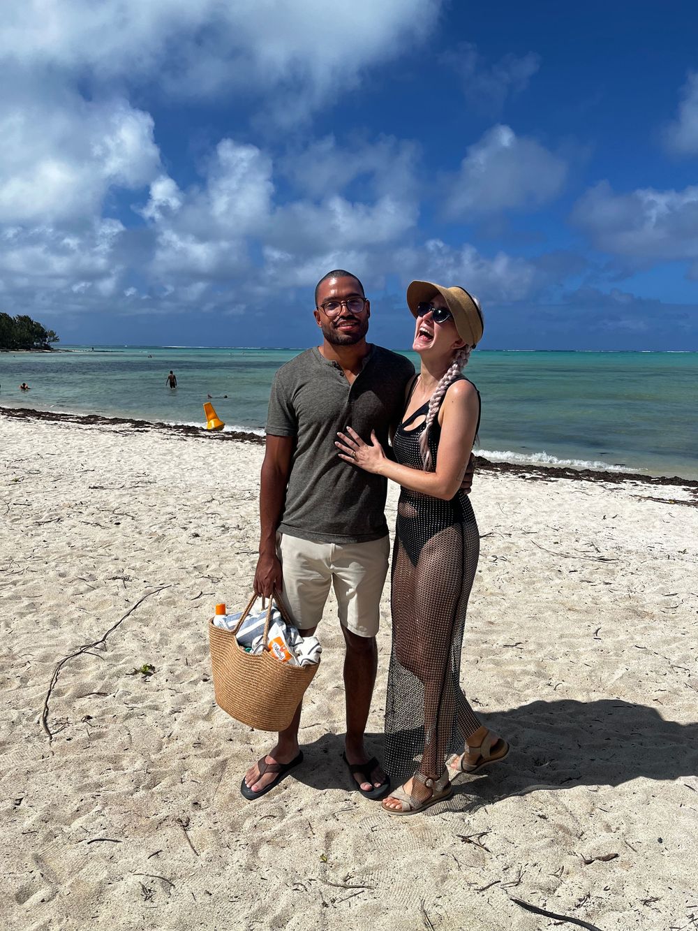 Couple sitting together on a white sandy beach with turquoise waters and blue skies in the background.