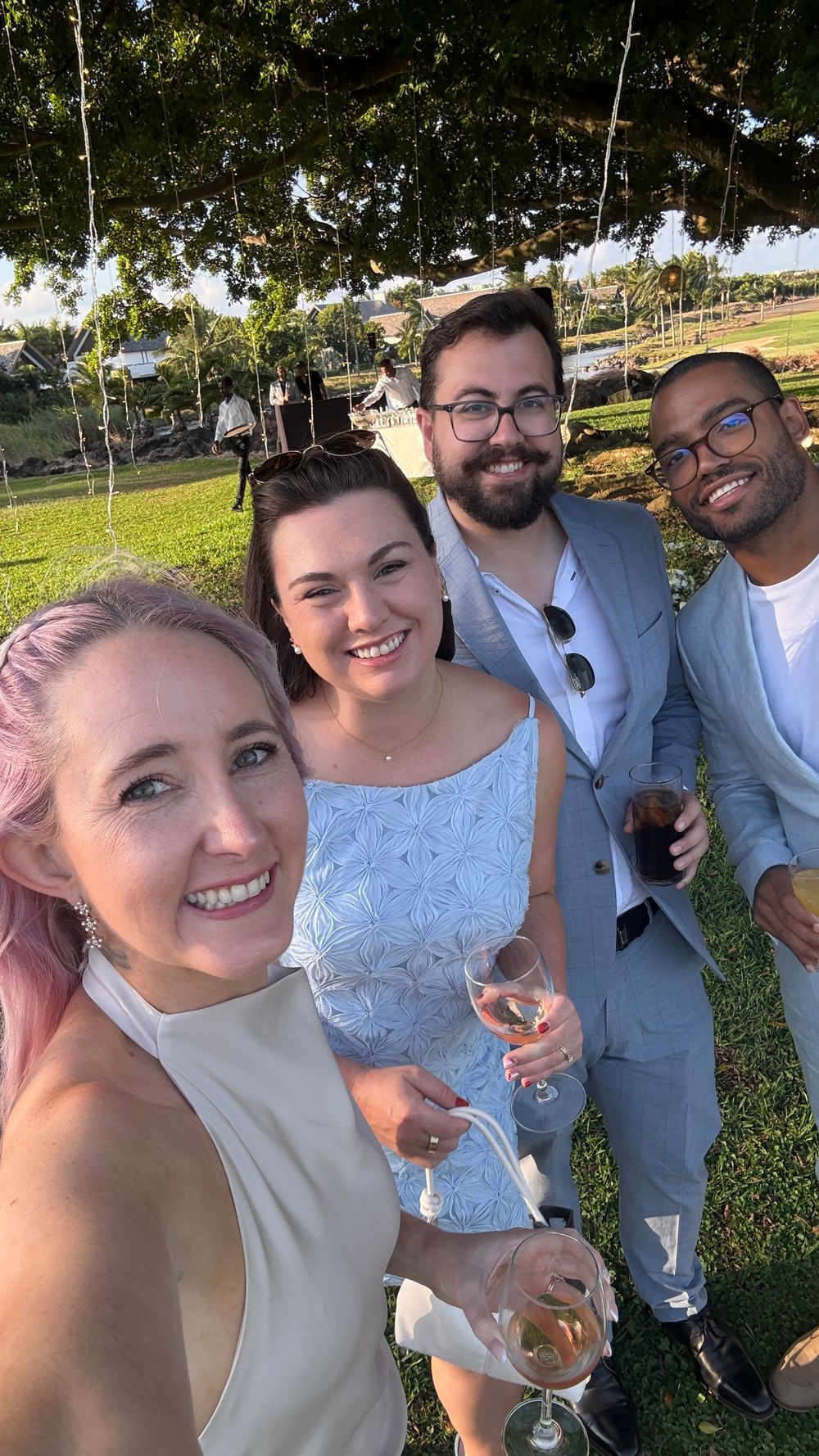 A group of friends enjoying drinks and smiling together at an outdoor event on a sunny day.