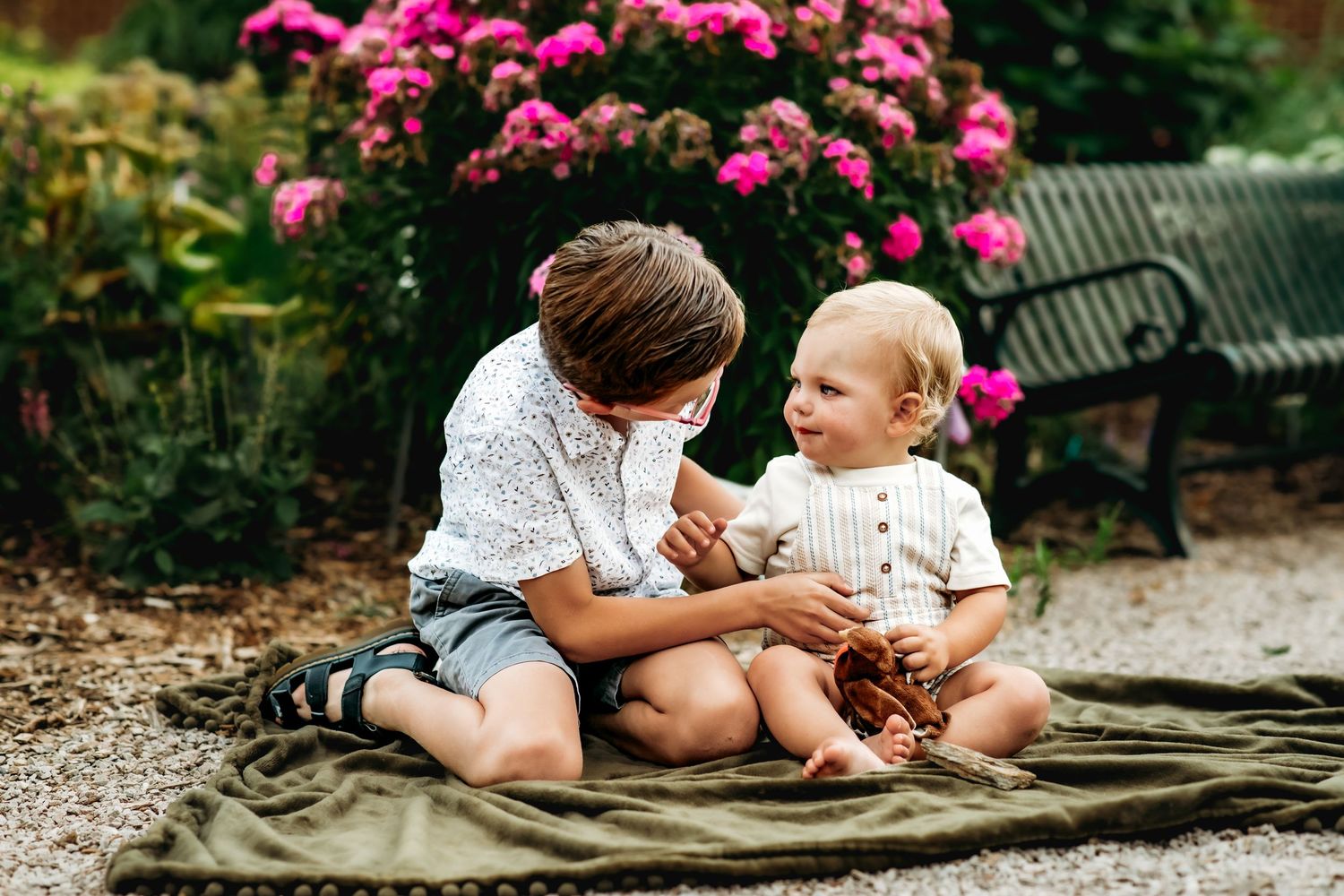 Two people share a tender moment on a blanket in a garden with vibrant pink flowers in the background.