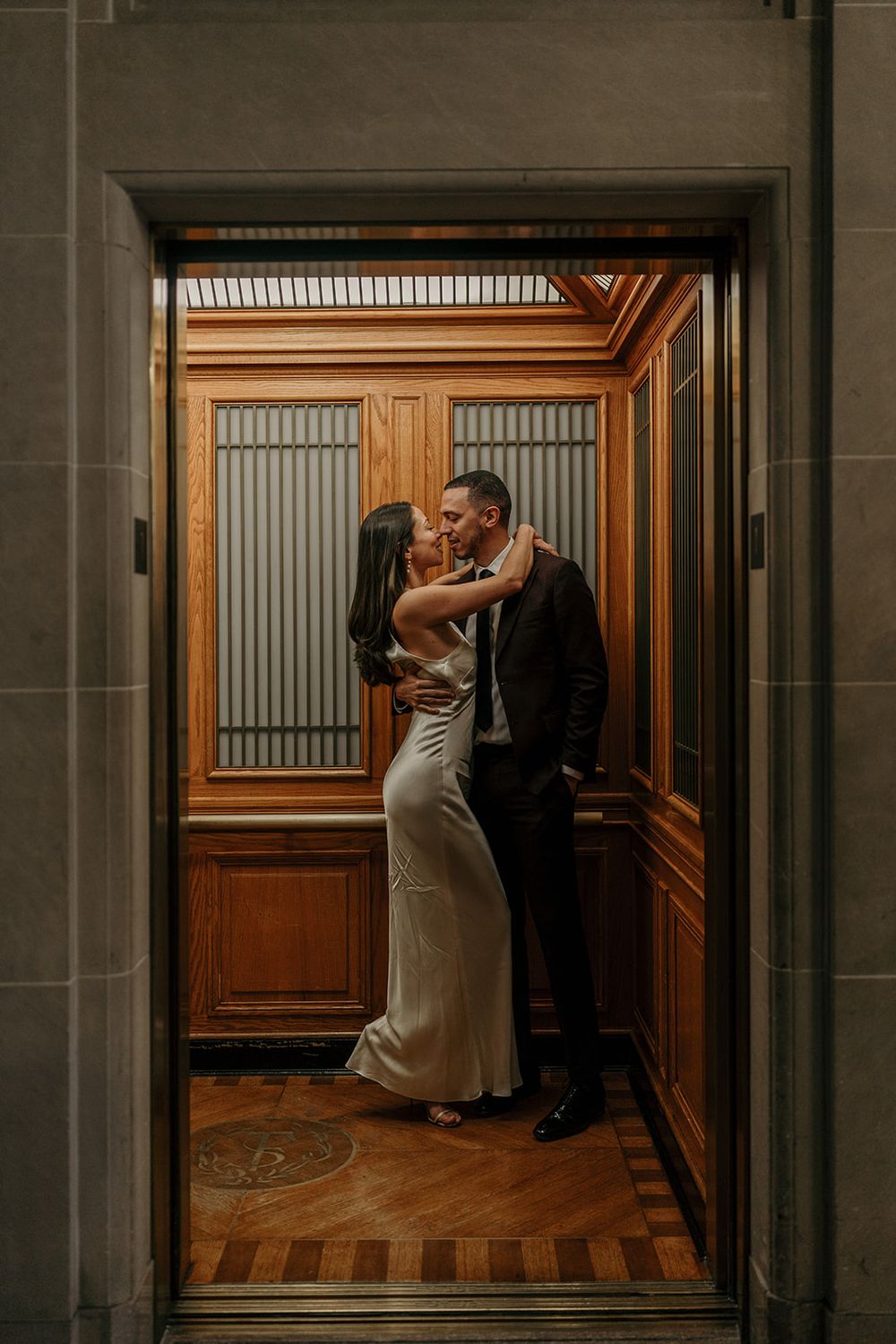 A romantic moment captured in a dimly lit hallway with wooden floors and elegant architectural details.