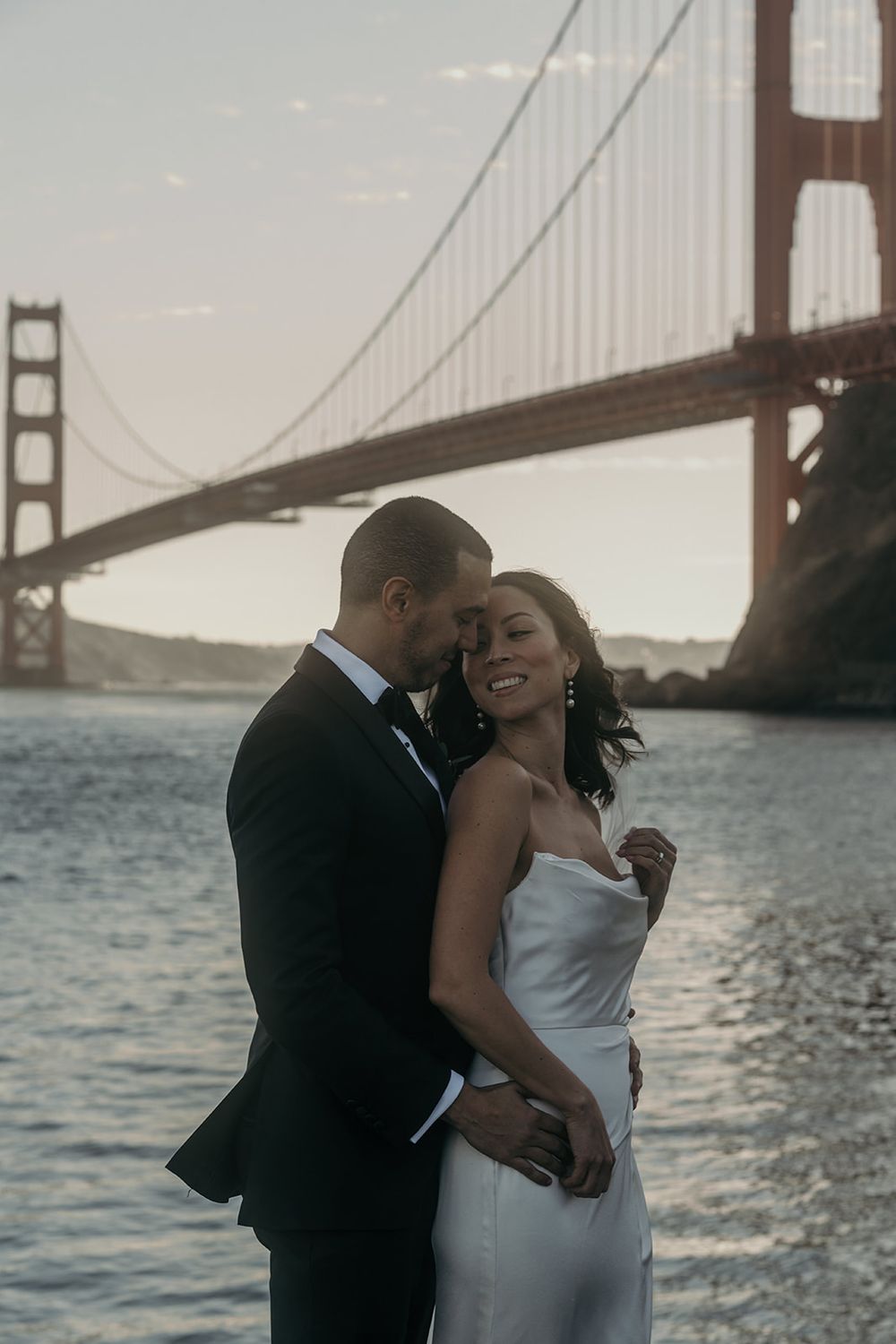 A couple shares romantic moments near the Golden Gate Bridge during sunset in San Francisco.