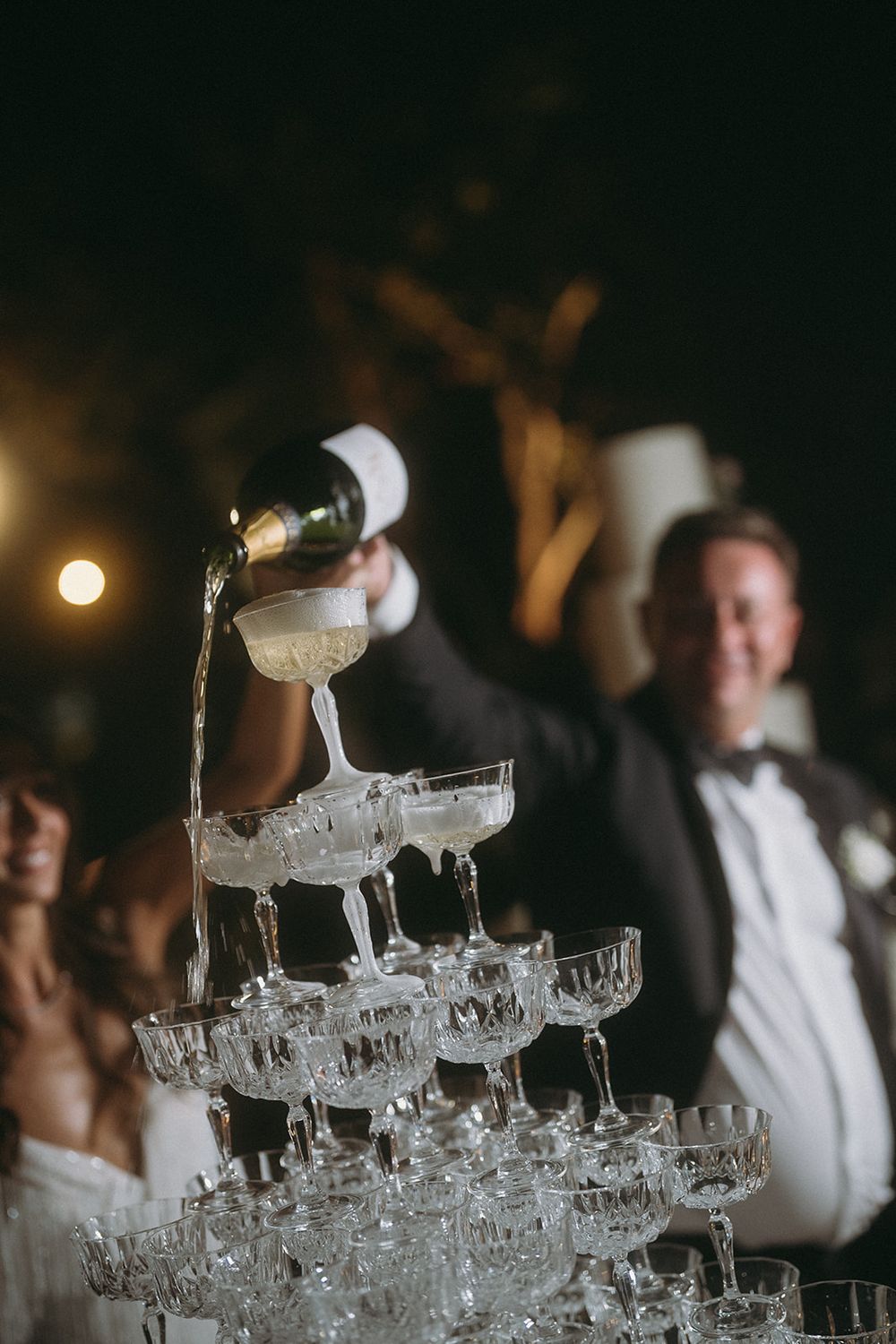 Crystal champagne glasses stacked in a pyramid formation at a formal celebration.