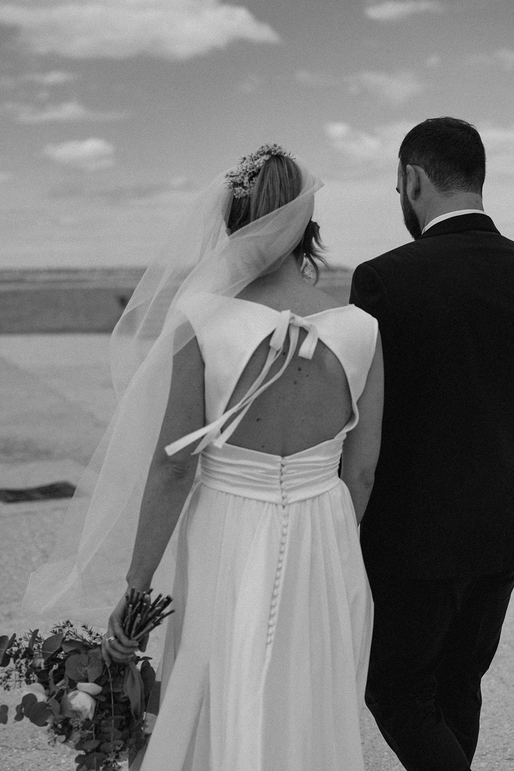 Black and white wedding photos show couple from behind in beach setting with bride in white dress and groom in dark suit.