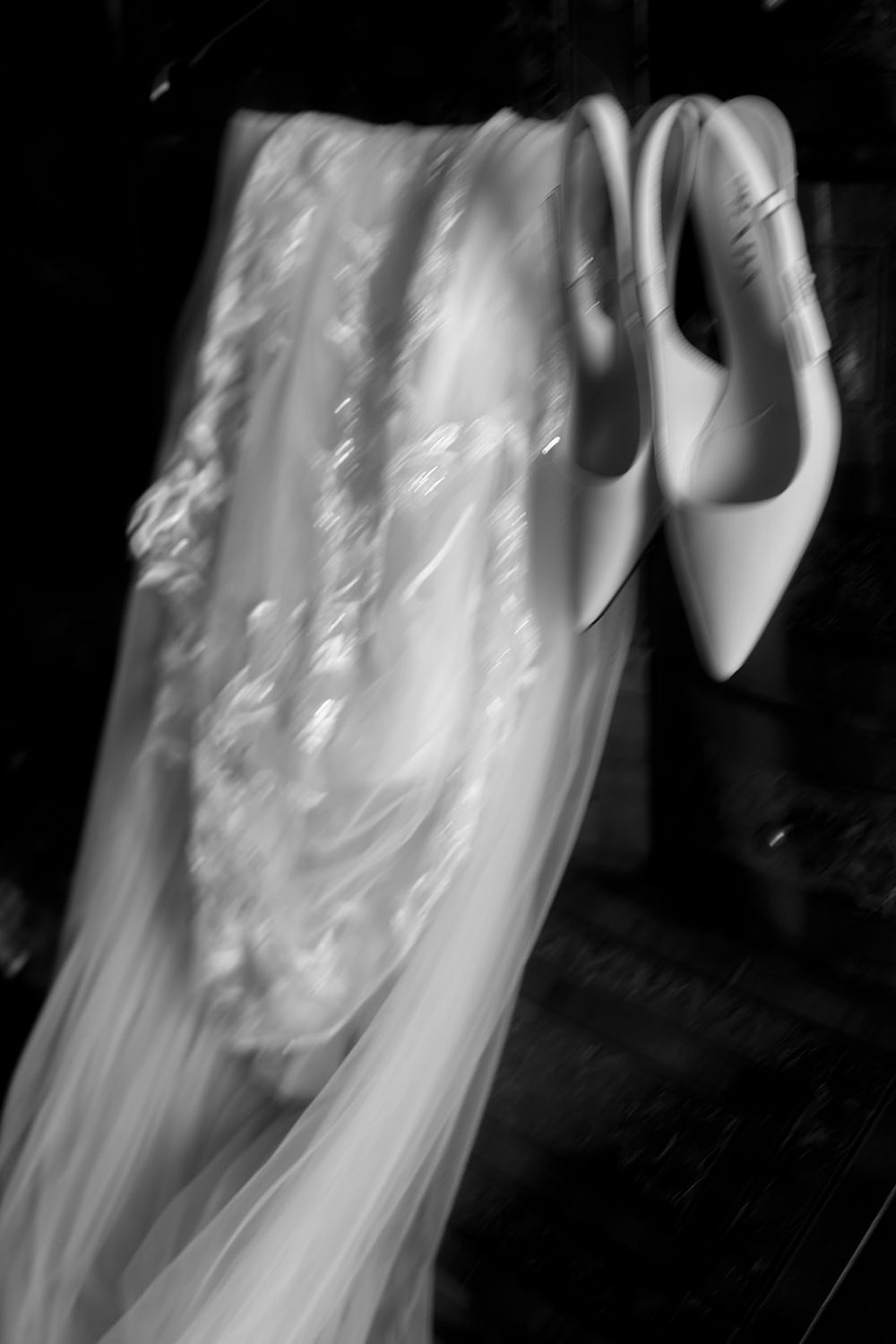 White bridal shoes and delicate lace veil arranged artistically in black and white photography.