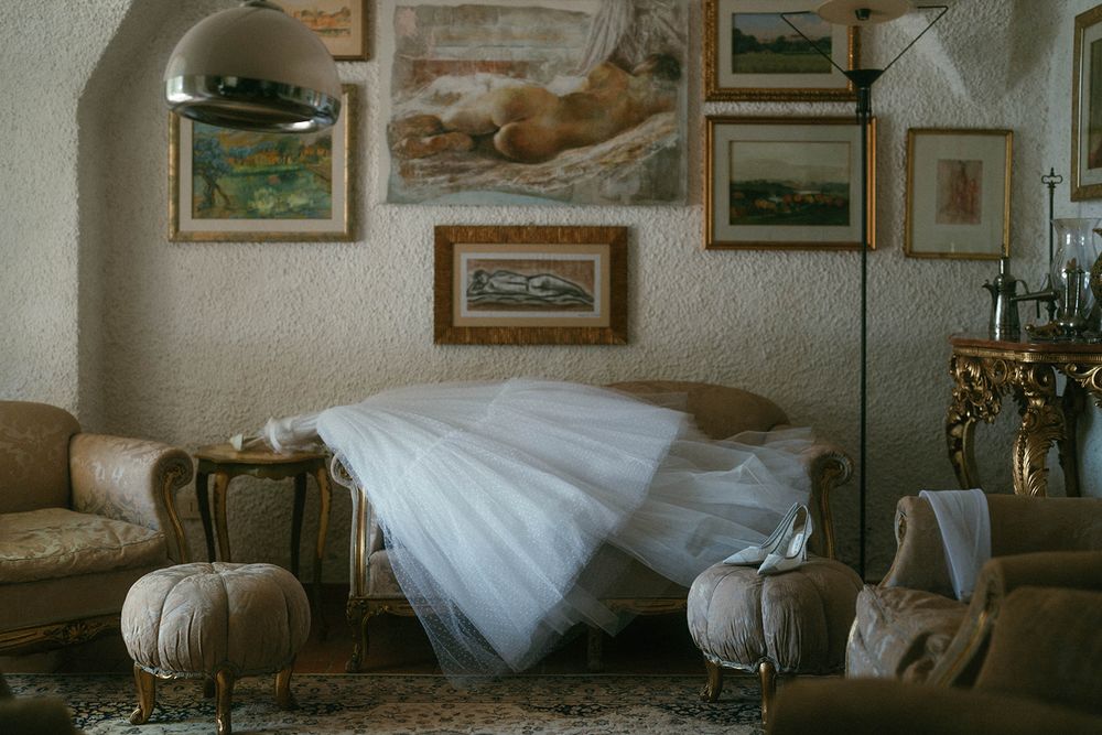 A vintage-style bedroom interior with framed artwork on walls, white bedding, and antique furnishings.
