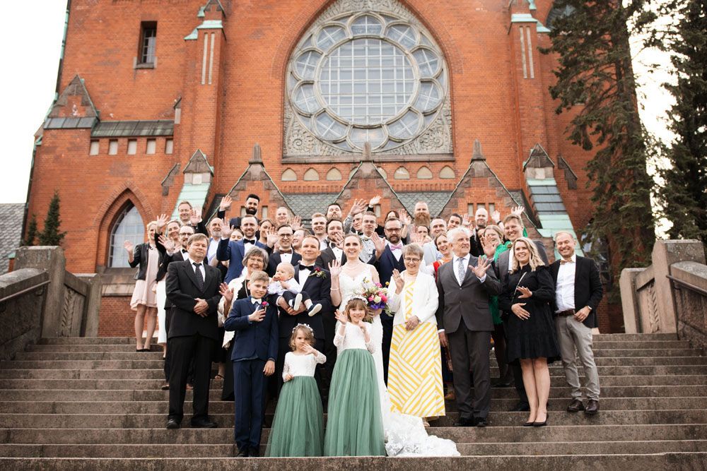 Hääseurue seisoo Mikaelin kirkon portaikossa ja vilkuttaa iloisesti kameralle. Edessä on morsian ja sulhanen sekä kaksi tyttöä.
