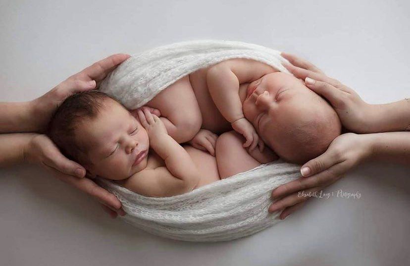 A series of soft black and white photos showing gentle hands cradling a sleeping newborn baby wrapped in white fabric.